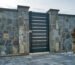 Pagar rumah batu alam gaya modern dengan pintu besi berwarna anthracite dan halaman berbatu — contoh desain fasad hunian yang kuat dan elegan