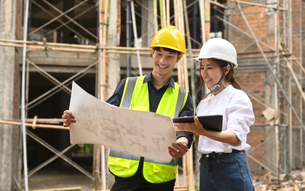 Dua pekerja konstruksi memeriksa gambar kerja di lokasi proyek sebagai ilustrasi kesalahan bangun rumah
