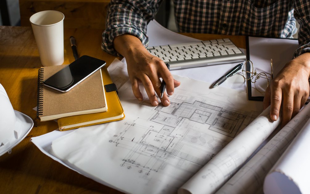 Tangan arsitek sedang mengerjakan gambar kerja denah rumah di meja studio, ilustrasi perencanaan profesional yang menjadi nilai harga jasa arsitek