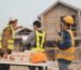 Tim arsitek jasa desain rumah Bogor sedang berdiskusi di lokasi proyek dengan maket rumah, gambar kerja, dan tablet untuk koordinasi konstruksi