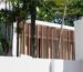 Fasad desain rumah modern tropis dengan secondary skin kayu vertikal dan vegetasi tropis di sekelilingnya
