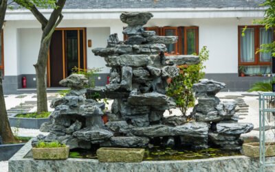 Water feature dari susunan batu alam di taman rumah dengan latar bangunan tropis tradisional