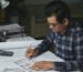 Arsitek profesional mengerjakan denah rumah dengan kalkulator dan referensi, ilustrasi cara memilih jasa arsitek rumah yang tepat
