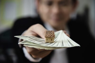 Ilustrasi konsep RAB rumah dengan miniatur rumah dan uang yang mencerminkan estimasi biaya pembangunan