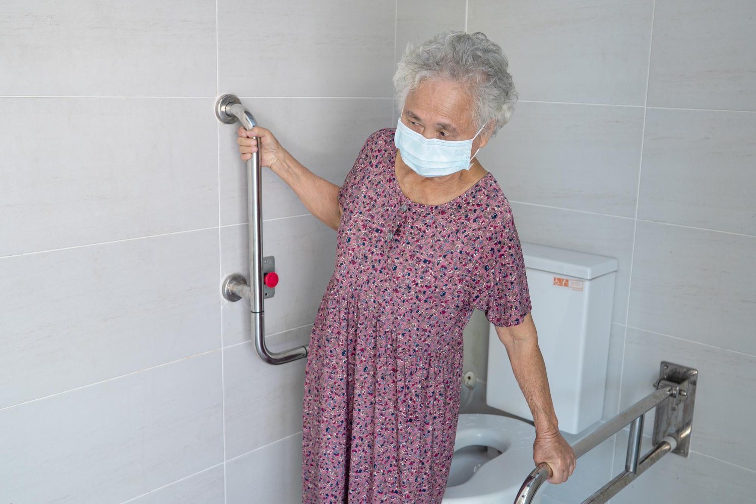 Lansia perempuan sedang memegang handrail di kamar mandi lansia yang dirancang aman untuk mengurangi risiko terpeleset